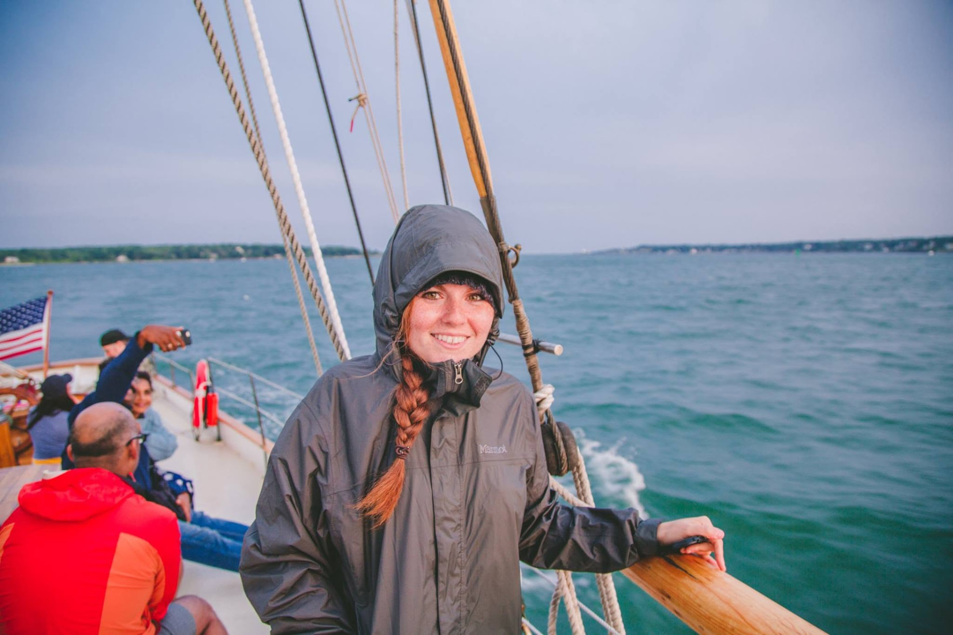 A girl in a rain jacket smiling at the rail of a sailing schooner